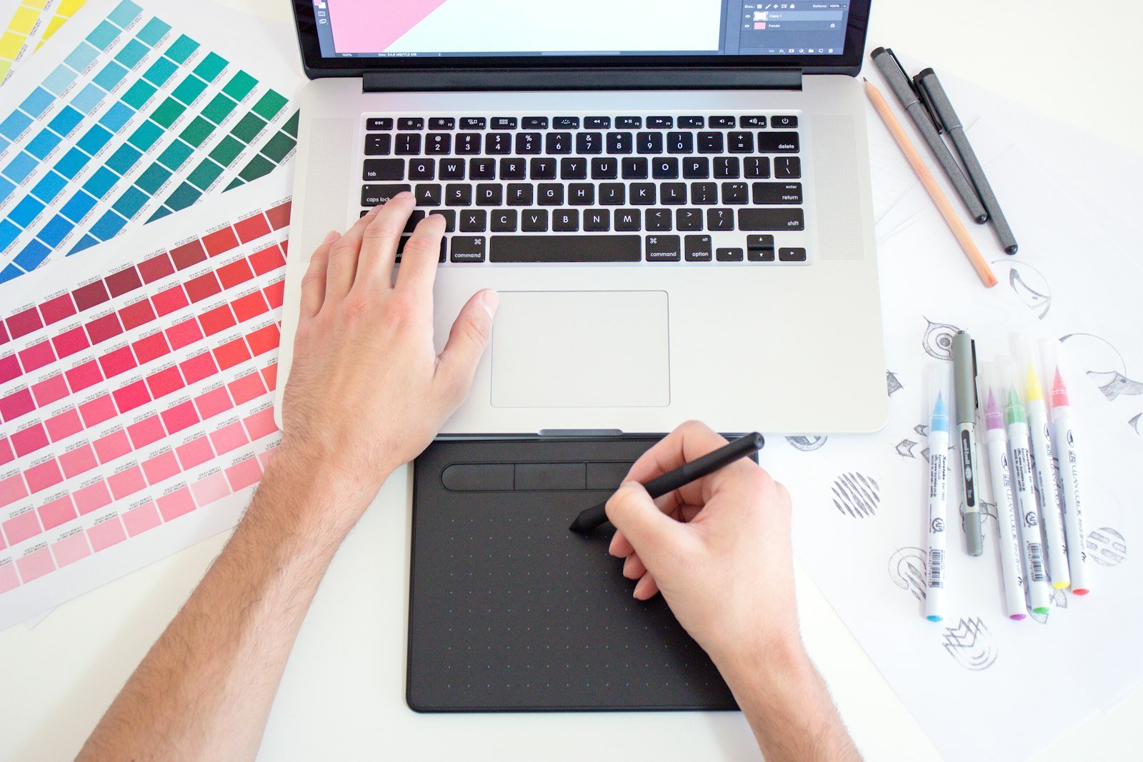 Hands sketching on a graphics tablet beside color swatches