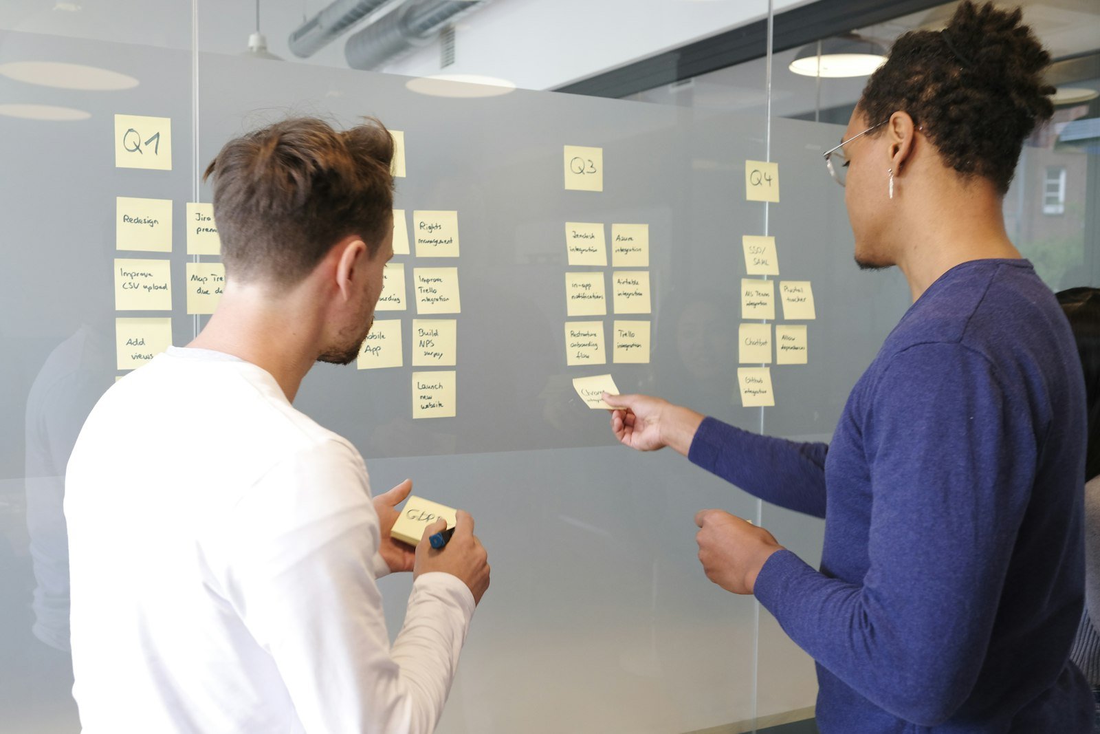 Two colleagues arranging planning notes on a glass wall